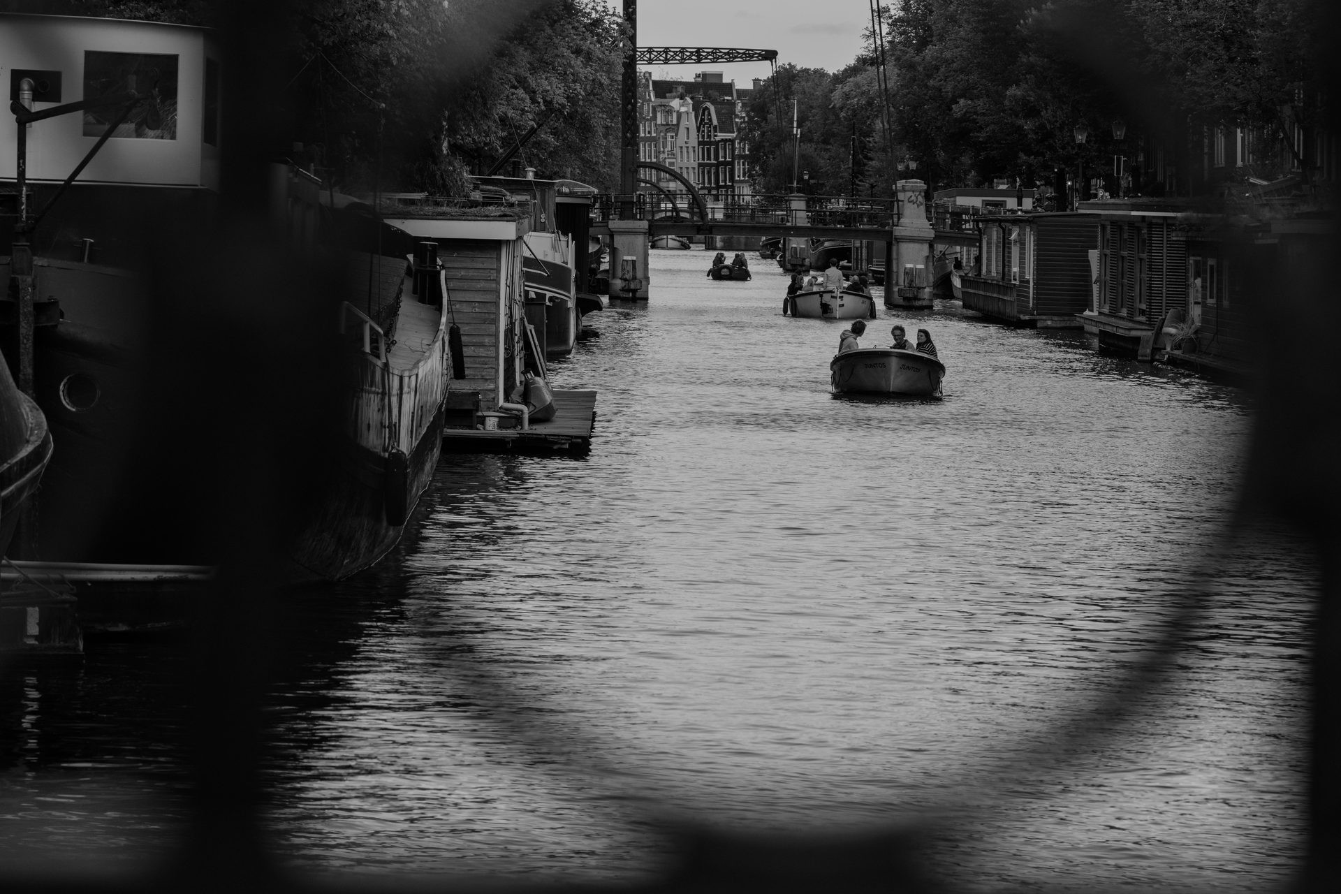 Amsterdam canal at dusk, moored houseboats and a small boat, drawbridge in the distance, black and white