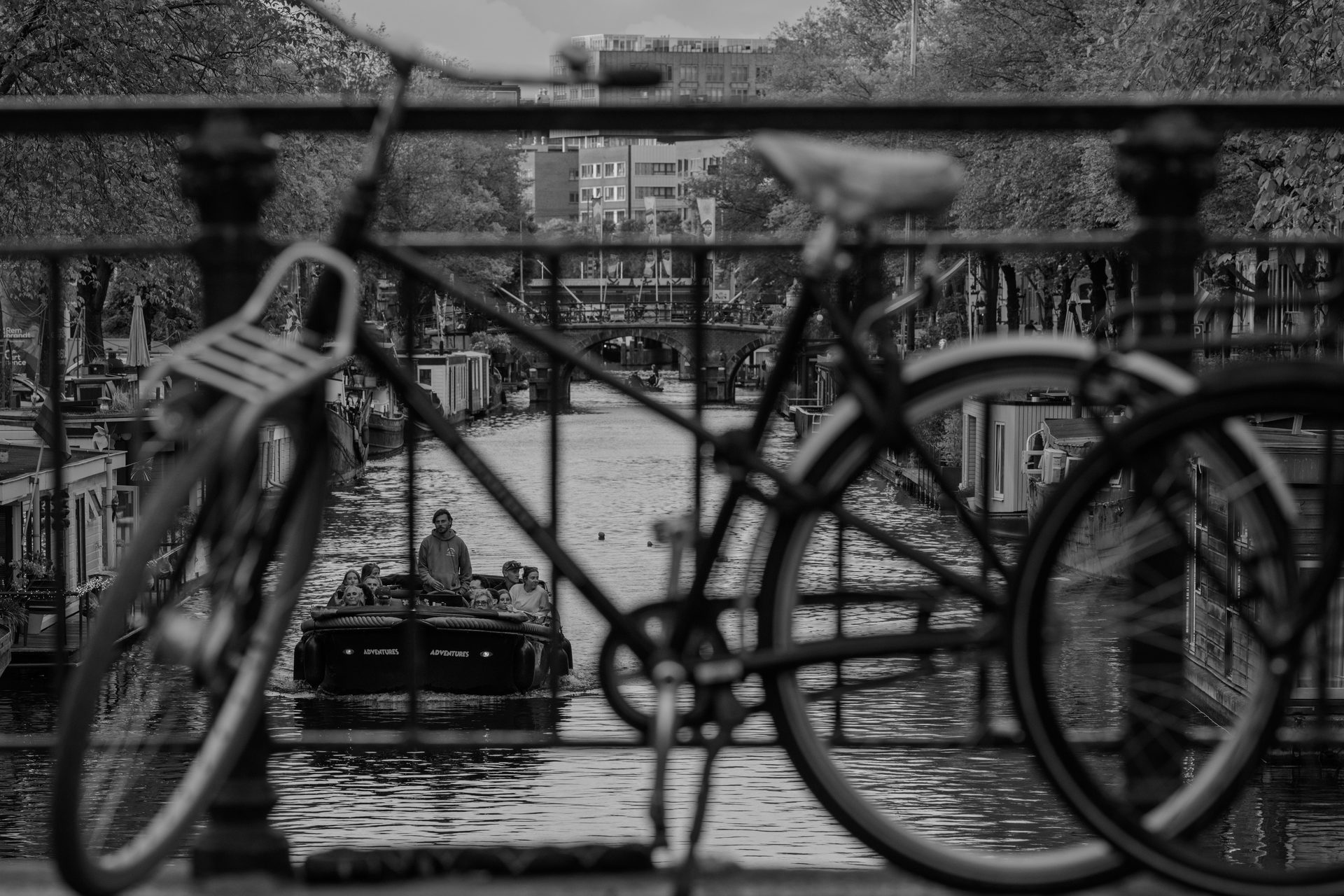 Bicycle silhouetted on a bridge railing, tour boat passing below, black and white